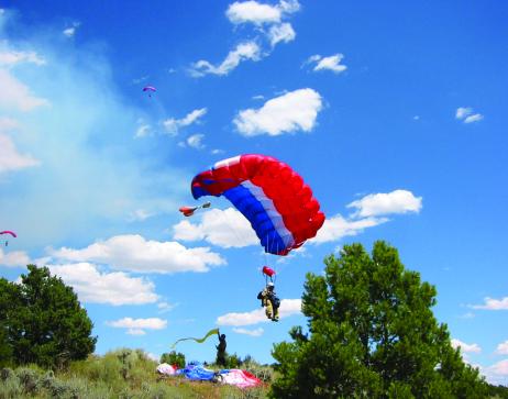 Bureau of Land Management Smokejumpers in Parachutes landing in a grassy field with low trees