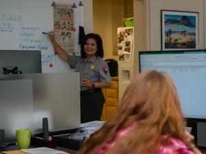 Woman instructor in front of whiteboard teaching another woman in front of a computer