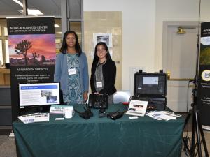 Two female contracting officers from the DOI Interior Business Center at a display table