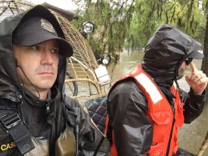 U.S. Fish and Wildlife Law Enforcement Officers dressed for stormy weather ride over flooded areas in an air boat.