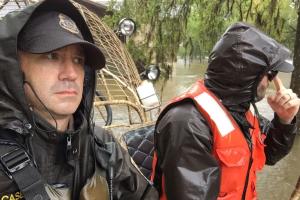 U.S. Fish and Wildlife Law Enforcement Officers dressed for stormy weather ride over flooded areas in an air boat.